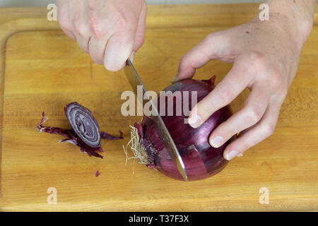 Close up of female slicing ends off of a red onion on a cutting board. Stock Photo