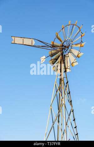 Low angle view of an old-fashioned, multi-bladed, metal wind pump on top of a lattice tower against blue sky. Stock Photo