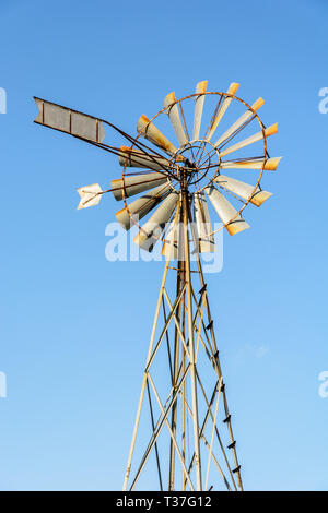 Low angle view of an old-fashioned, multi-bladed, metal wind pump on top of a lattice tower against blue sky. Stock Photo