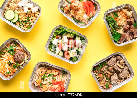 Daily meals in foil boxes on yellow background, top view, flat lay. Healthy food delivery concept. Fitness nutrition for diet. Stock Photo