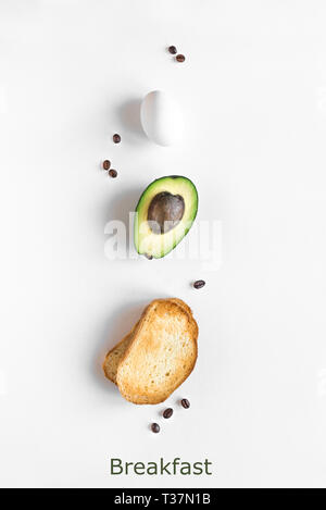 Avocado, egg and toast for breakfast on white background, top view, copy space. Healthy breakfast ingredients - egg, bread, avocado and coffee beans. Stock Photo
