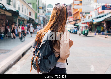 Rear view of young female tourist backpacker walking on Khao San road in summer during trip to Bangkok, Thailand Stock Photo