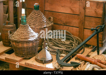 Composition with old wooden cart and wine flasks with old rope and anchor in Italy Stock Photo