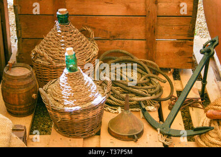 Composition with old wooden cart and wine flasks with old rope and anchor in Italy Stock Photo