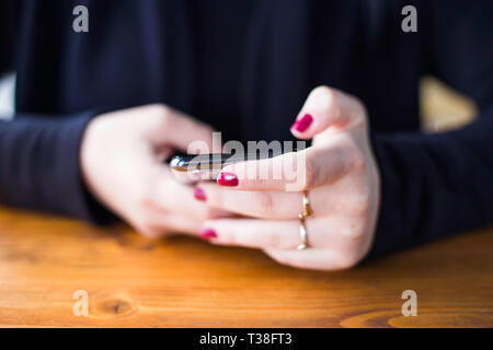 Woman in black shirt typing on smart phone in cafe, no face, close up, red fingers, communication concept Stock Photo