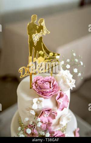 Wedding cake with white and pink sugar flowers and gold topper Stock Photo