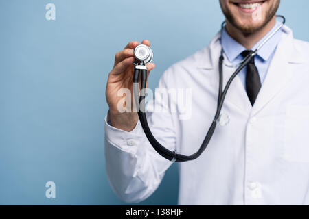 Handsome young medic holding a stethoscope, isolated over light blue.