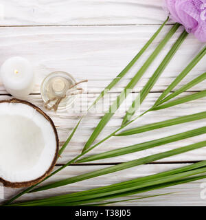 Flat lay Coconut oil in glass bottle bath sponge candle and shell pieces on white wooden table Stock Photo