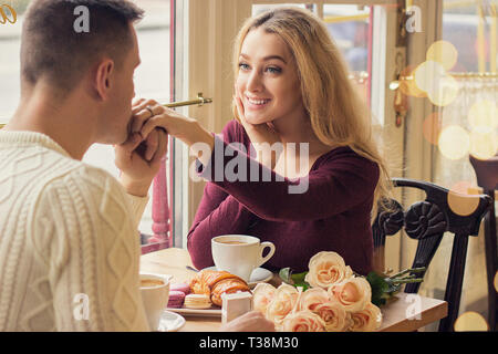 Back view man kissing his beloved woman hand while having romantic dinner in cozy french cafe. Happy young couple celebrating in vintage restaurant. V Stock Photo