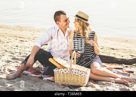 Happy to be together. Horizontal shot of cheerful beautiful young couple sitting looking at each other while having romantic picnic on beach. Woman op Stock Photo