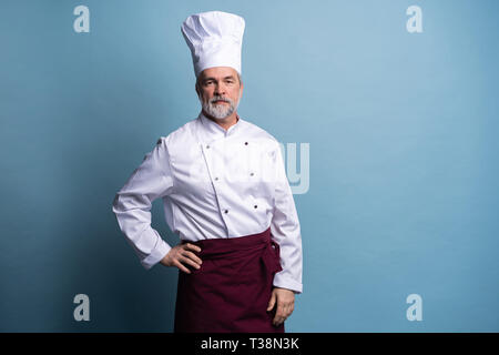 Attractive smiling cheerful chef isolated on blue. Stock Photo
