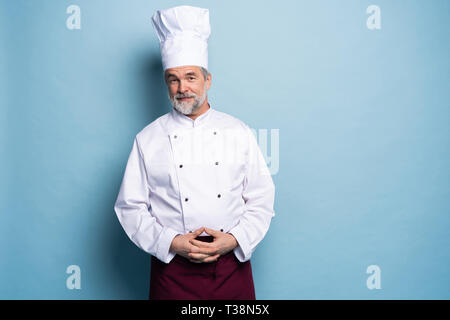 Attractive smiling cheerful chef isolated on blue. Stock Photo