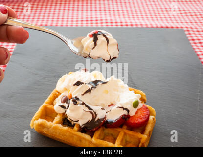 Taking a tablespoon of cream in a waffle with strawberries, whipped cream, chocolate syrup and candy colors Stock Photo