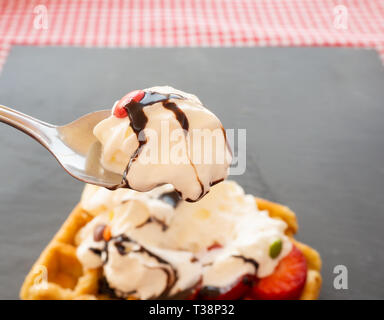 Taking a tablespoon of cream in a waffle with strawberries, whipped cream, chocolate syrup and candy colors Stock Photo