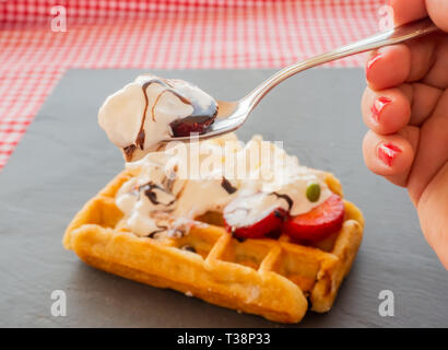 Taking a tablespoon of cream in a waffle with strawberries, whipped cream, chocolate syrup and candy colors Stock Photo