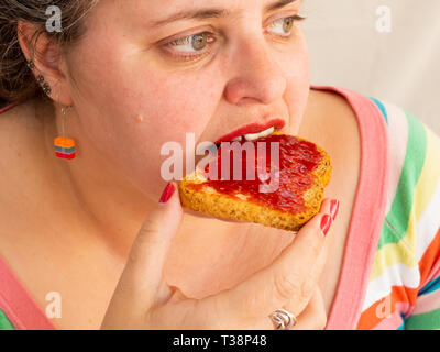 An adult woman with red nails and lips eating a rusk with raspberry jam Stock Photo