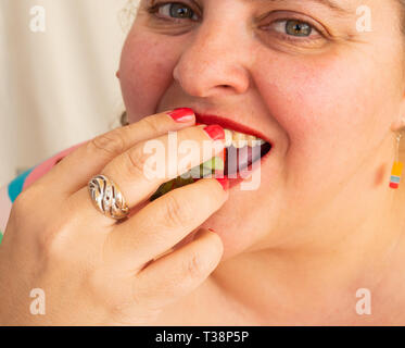 An adult woman with red nails and lips eating a strawberry Stock Photo