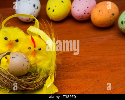 Colorful easter eggs with chickens nest on brown wooden table, easter postcard Stock Photo