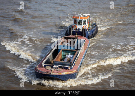 Looking down at a tugboat pushing a large cargo barge carrying waste materials down the river, taken on the river Thames in London 26th of April 2019 Stock Photo