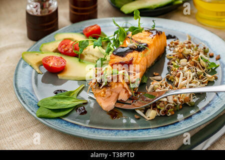 A piece of baked red fish with a side dish of sprouts and avocado salad. Macrobiotic food concept. Healthy food. Stock Photo