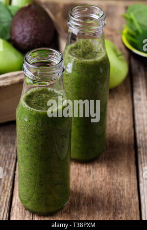 Healthy green fruits and vegetables smoothie in bottles on rustic wooden table, spinach, avocado, apple, celery and lime juice drink with ingredients, Stock Photo