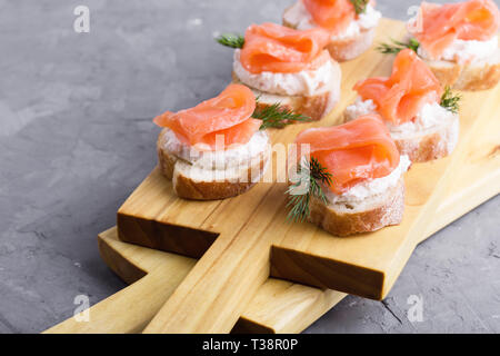 Party food, appetizer with salmon pate and smoked salmon on wooden cutting board, snack platter on gray background close-up, selective focus Stock Photo