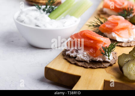 Party food, appetizer with salmon pate and smoked salmon, yoghurt dip with dill, celery sticks and pickles on wooden board, snack platter close-up, se Stock Photo
