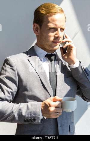 Portrait of a young business man talking on smartphone and holding cup of coffee Stock Photo