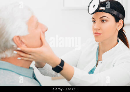 otolaryngologist doctor examining her patient, checking seniors man nose at clinic Stock Photo