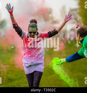 Adult female runner with arms held high being covered in paint on Macmillan cancer charity 5K color fun run. Stock Photo