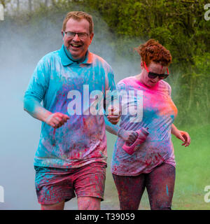 Adult couple running and laughing and being covered in paint on Macmillan cancer charity 5K color fun run. Stock Photo