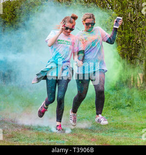 Two women runners, one holding a smart phone, being covered in paint on Macmillan cancer charity 5K color fun run. Stock Photo