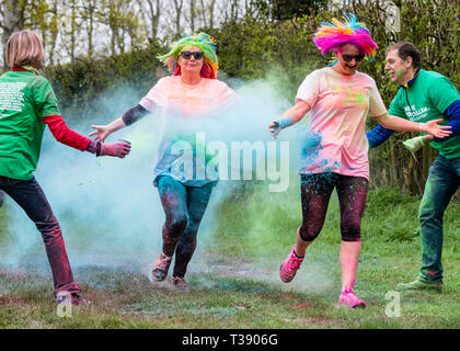 Two women with coloured wigs being covered in paint on Macmillan cancer charity 5K colour fun run. Stock Photo