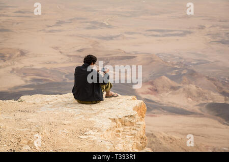 Mitzpe Ramon, Israel - 22 november, 2016: Man is taking a picture with a smartphone on the edge of Ramon crater cliff at  Negev desert, Israel Stock Photo