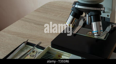 Microscope on the desk of the biologist with the micro-specimens, a scalpel and tweezers. Stock Photo