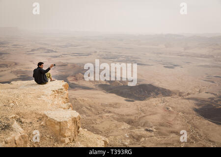 Mitzpe Ramon, Israel - 22 november, 2016: Man is taking a picture with a smartphone on the edge of Ramon crater cliff at  Negev desert, Israel Stock Photo