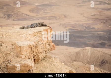 Mitzpe Ramon, Israel - 22 november, 2016: Man is lying on the edge of Ramon crater cliff at  Negev desert, Israel Stock Photo