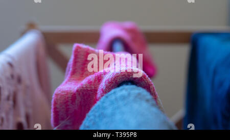 Macro photography close up shot of woven pink (magenta) ankle sock drying on a laundry rack indoors. Background blur, center selective focus. Stock Photo