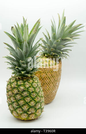 two standing pineapples with one in a basket on an isolated white background Stock Photo
