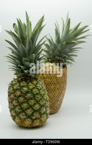 two standing pineapples with one in a basket on an isolated white background Stock Photo