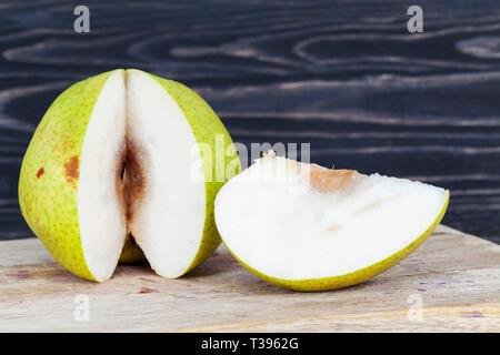 Cut into pieces a large pear rotted inside in the heart Where are the seeds, cut on the cutting board, spoiled fruit Stock Photo