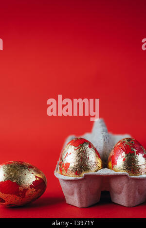Group of golden colored and decorated with sparkles Easter eggs. Easter egg hunt celebration, colorful still life in paper box on red background. Stock Photo