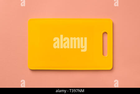 Colored yellow plastic cutting board on pink background, top view. Stock Photo
