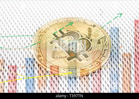 Golden Bitcoin, cryptocurrency physical coin and defocused chart foreground. Virtual cryptocurrency concept Stock Photo