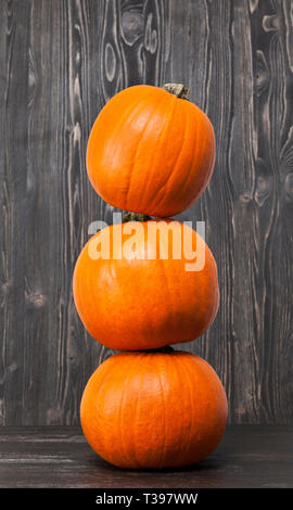 lying on top of each other Three small orange pumpkins on a wooden floor in black against a black wall of wood Stock Photo