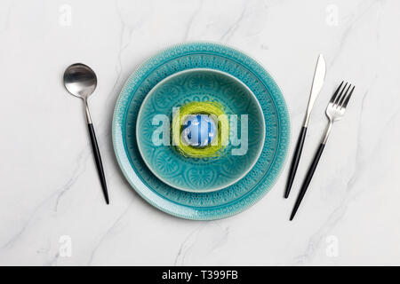 Elegance table setting spring with green nest on light marble. Easter egg in nest on plate with tableware. Easter romantic dinner. Top view. Concept o Stock Photo