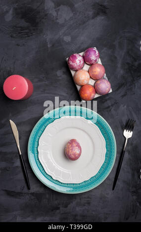 Serving plate for Easter and other holidays. Fork and knife on white and blue plates, pink egg on plate at dark background, Eggs holder and pink candl Stock Photo