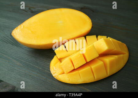 Vibrant Yellow Fresh Ripe Thai Nam Dok Mai Mango Cut in Half on Dark Brown Wooden Table Stock Photo