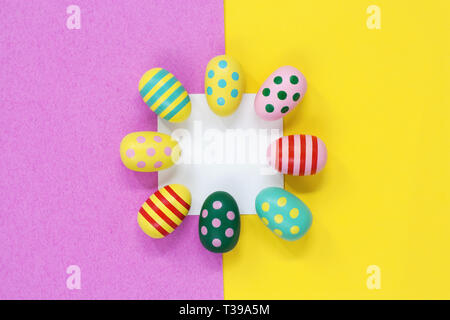 Brightly coloured Easter eggs around a blank white square of paper, on a pink and yellow background Stock Photo