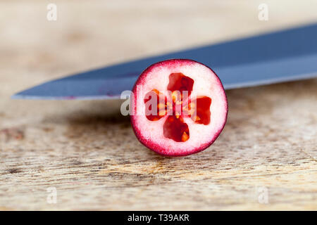 Cut in the middle ripe large cranberries grown in the swamp, on a natural wooden surface Stock Photo